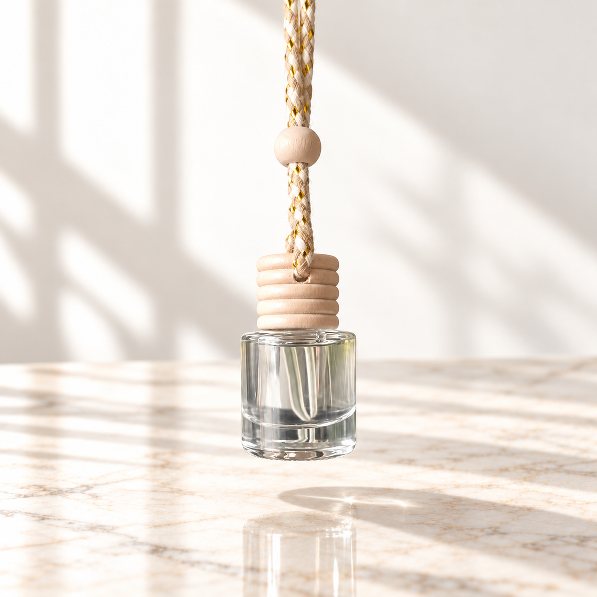 Clear glass car diffuser with natural wood cap and braided cord, hanging above ivory marble against a white background